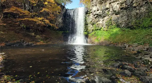 La cascade d'Entraigues, un rideau d'eau tombant dans un bassin entouré de roches et de feuillages d'automne aux couleurs vives.