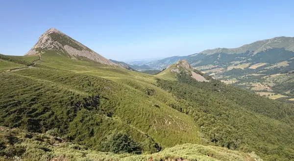 Vue panoramique sur le Puy Griou, sommet emblématique du Cantal, avec ses pentes verdoyantes et rocheuses sous un ciel bleu.