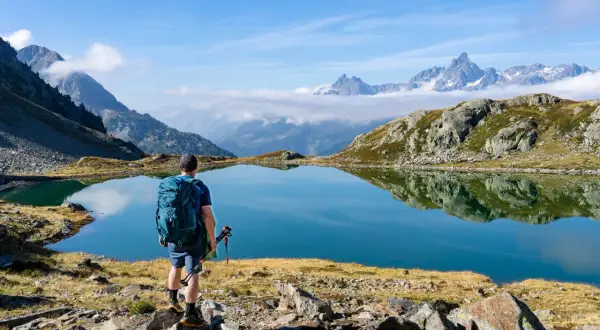 Randonneur contemplant un lac d'altitude aux reflets parfaits, paysage du tour des lacs des 7 Laux.