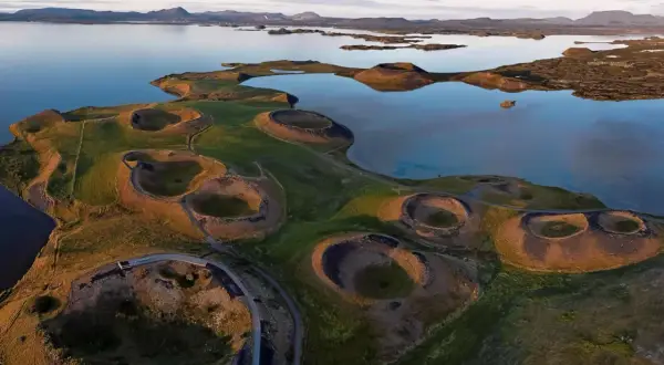 Paysage spectaculaire du lac Myvatn en Islande, avec ses cratères volcaniques verdoyants et ses eaux calmes reflétant le ciel.