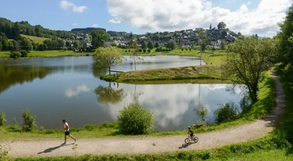 Un homme court sur le sentier, un enfant fait du vélo près du lac tour d'auvergne. Village en arrière-plan.