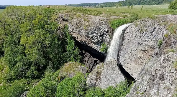 La cascade du Deroc, un lieu idéal pour la baignade, dévale une falaise rocheuse entourée de verdure.