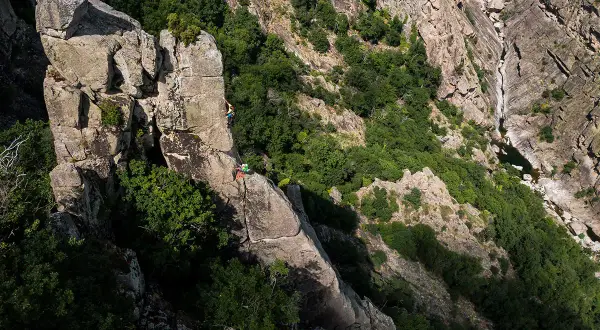 Escalade dans les gorges du Bramont. Deux grimpeurs évoluent sur un piton rocheux, entourés de végétation luxuriante.