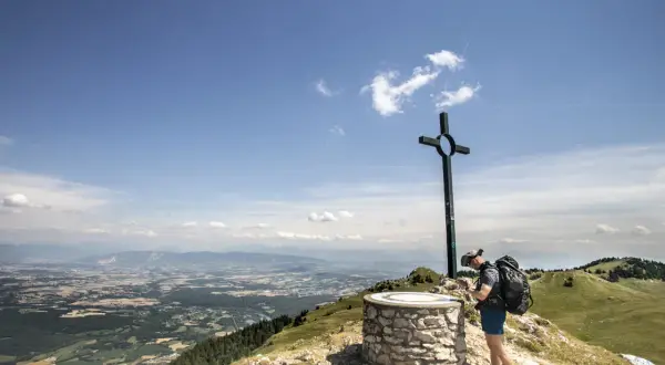 Fin d'une randonnée boucle 5 jours Jura. Un randonneur admire le panorama depuis un sommet, près d'une croix et d'un repère.