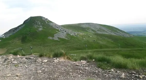 Vue panoramique du Puy de Paillaret, un volcan d'Auvergne aux pentes verdoyantes parsemées de roches.
