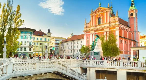 Pont triple de Ljubljana, un incontournable Slovénie, avec l'église franciscaine rose et des passants profitant du soleil.