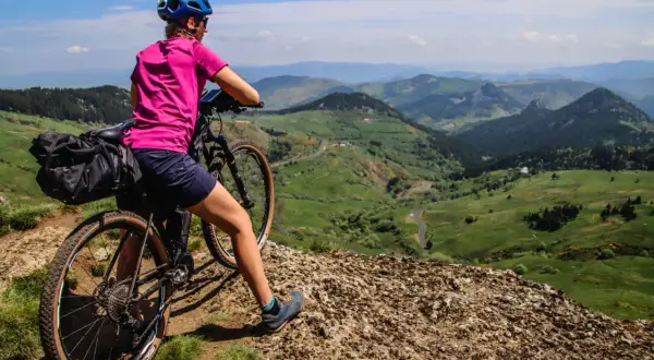 Cycliste au col de la Croix de Boutières, admirant le paysage verdoyant et vallonné. Sacoche sur le vélo, prête pour l'aventure.
