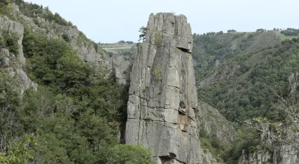 Un piton rocheux domine les gorges du Bes, entouré de végétation luxuriante et de falaises escarpées.