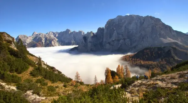 Vue spectaculaire des Alpes Juliennes, avec une mer de nuages enveloppant les vallées et des montagnes majestueuses sous un ciel bleu.