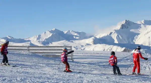 Enfants en plein cours de ski, profitant d'une journée ensoleillée avec des montagnes enneigées en arrière-plan.