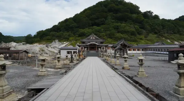 Allée de lanternes menant à un temple au pied du mont Osore, paysage volcanique et verdoyant.