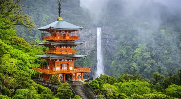 Pagode à trois étages de couleur orange vif, niché dans une végétation luxuriante sur la péninsule de Kii, avec une cascade majestueuse en arrière-plan.