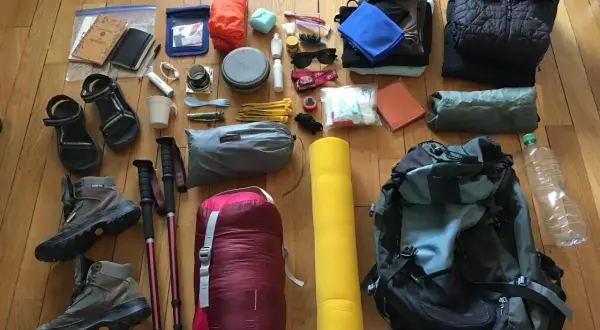 Préparation pour une aventure : chaussures de randonnée, sac de couchage, matelas, vêtements, gourde et accessoires pour savoir comment ranger son sac de randonnée.