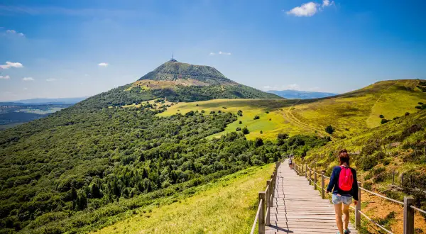 Une randonneuse sur un sentier en bois, profitant du paysage verdoyant du Massif Central. Le tourisme y est magnifique.