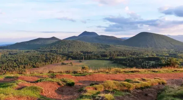Vue panoramique sur les volcans d'Auvergne, avec le Puy Chopine dominant la forêt verdoyante sous un ciel nuageux.