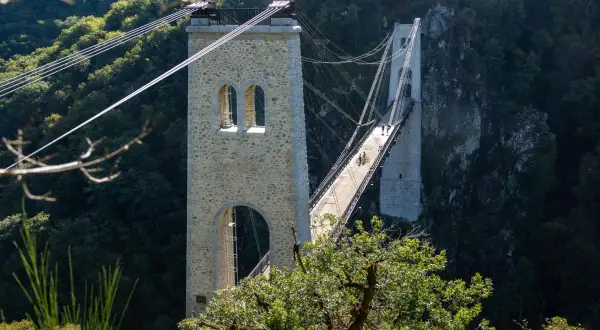 Le viaduc des Rochers Noirs, un pont suspendu impressionnant, traverse une vallée verdoyante. Deux personnes à vélo profitent de la vue.