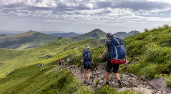 Randonneurs sur un sentier escarpé, dominant des paysages verdoyants et des volcans du puy May.