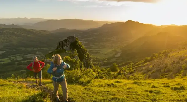 Deux randonneurs sur le sentier des cathares, profitant d'un paysage montagneux baigné par le soleil couchant.