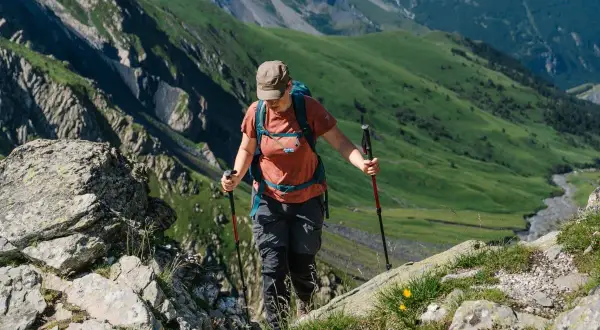 Randonneuse utilisant des bâtons pour gravir une pente rocheuse. Ces bâtons de marche servent à stabiliser et soulager les articulations en terrain accidenté.
