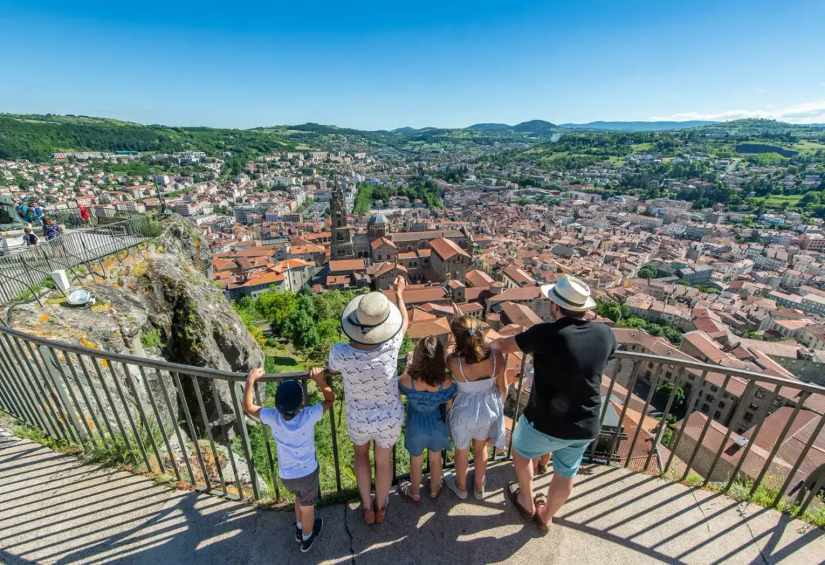 Une famille admire le panorama de la ville. Que voir au Puy en Velay ? La cathédrale et ses toits de tuiles rouges s'étendent à perte de vue.
