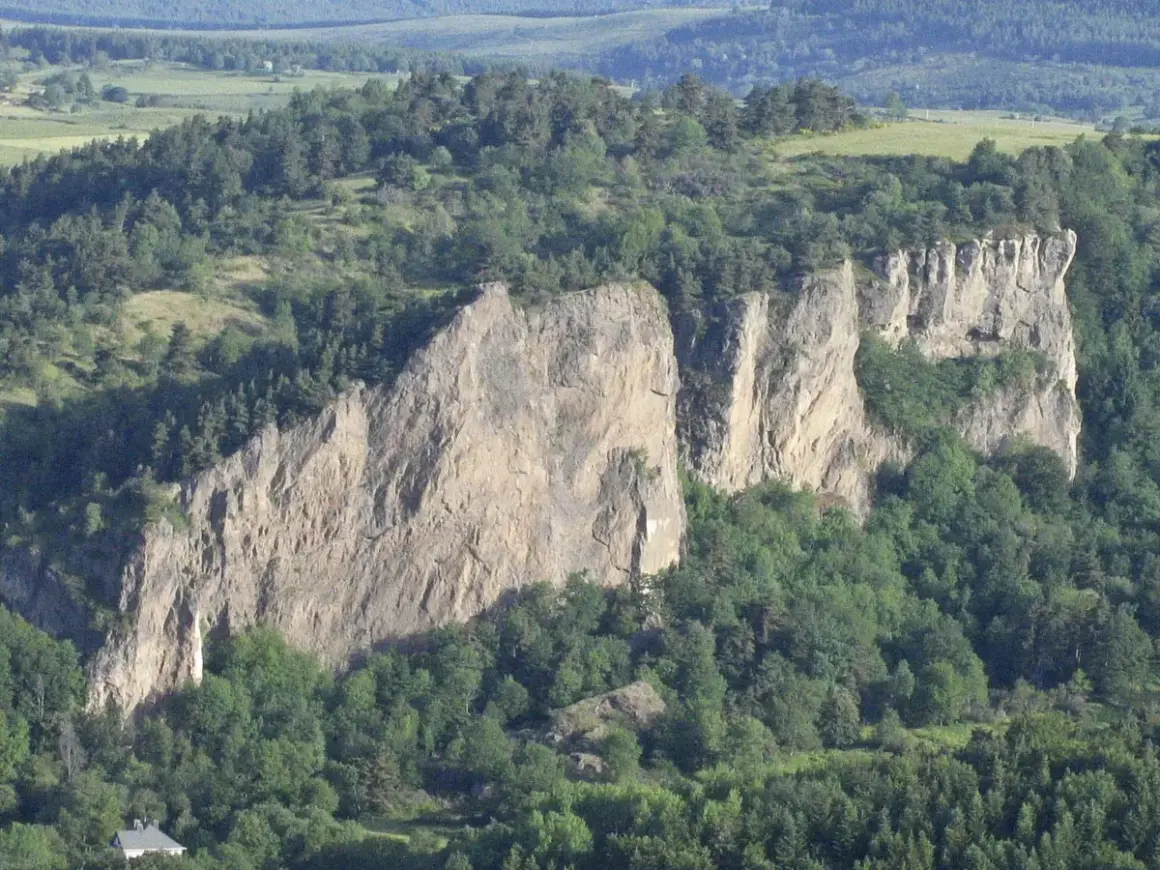 Falaises rocheuses spectaculaires, idéales pour une randonnée à Murol. Végétation luxuriante et paysage vallonné en arrière-plan.