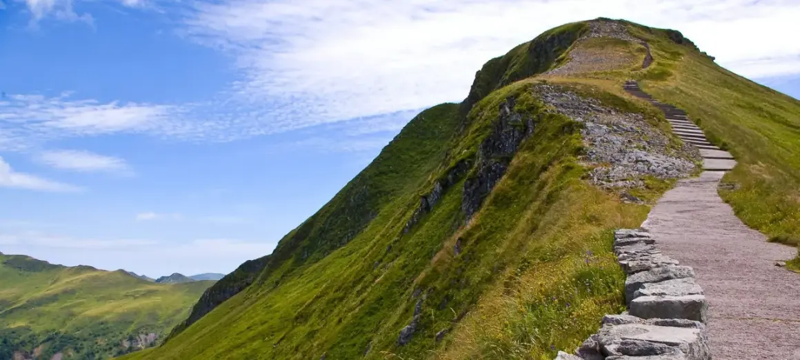 Sentier de montagne verdoyant avec escaliers, idéal pour une randonnée gr pour débutant. Paysage spectaculaire sous un ciel bleu.