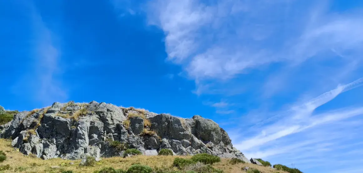Rochers escarpés du Puy de Niermont sous un ciel bleu éclatant, parsemé de nuages légers.