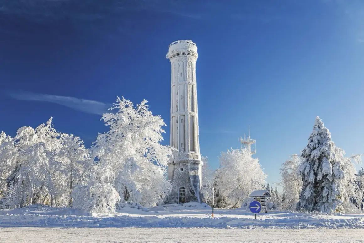 Tour de guet enneigée, tel un champ du feu blanc sous un ciel bleu intense. Arbres givrés et paysage hivernal.