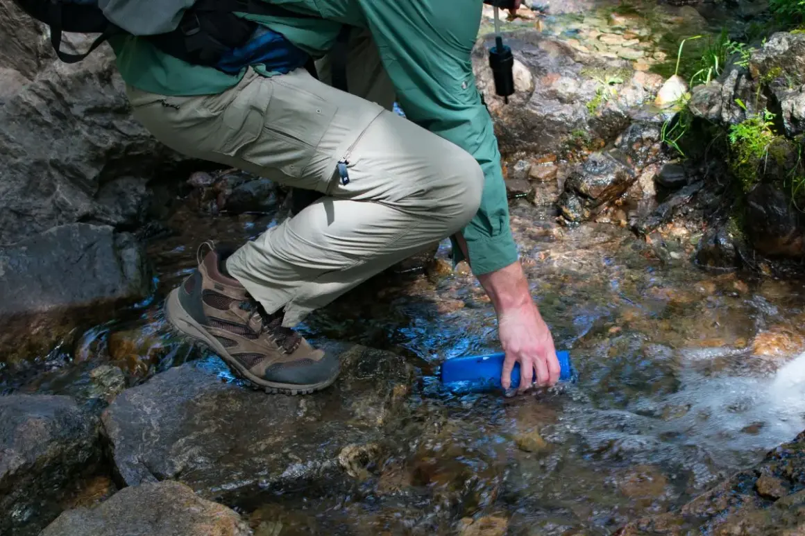Randonneur remplissant une gourde dans un ruisseau, prêt à utiliser une pastille de chlore pour eau potable.