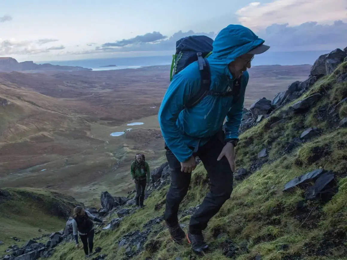 Randonneurs sur un sentier escarpé du Skye Trail, profitant d'un paysage spectaculaire avec des lacs et la mer en arrière-plan.