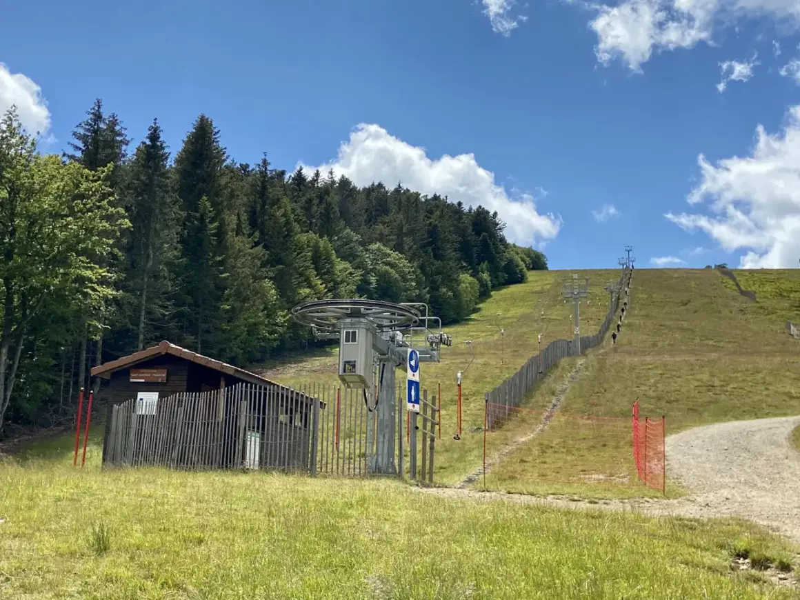 Remontée mécanique au col de Supeyres, avec une cabane en bois et une piste d'été bordée de sapins.