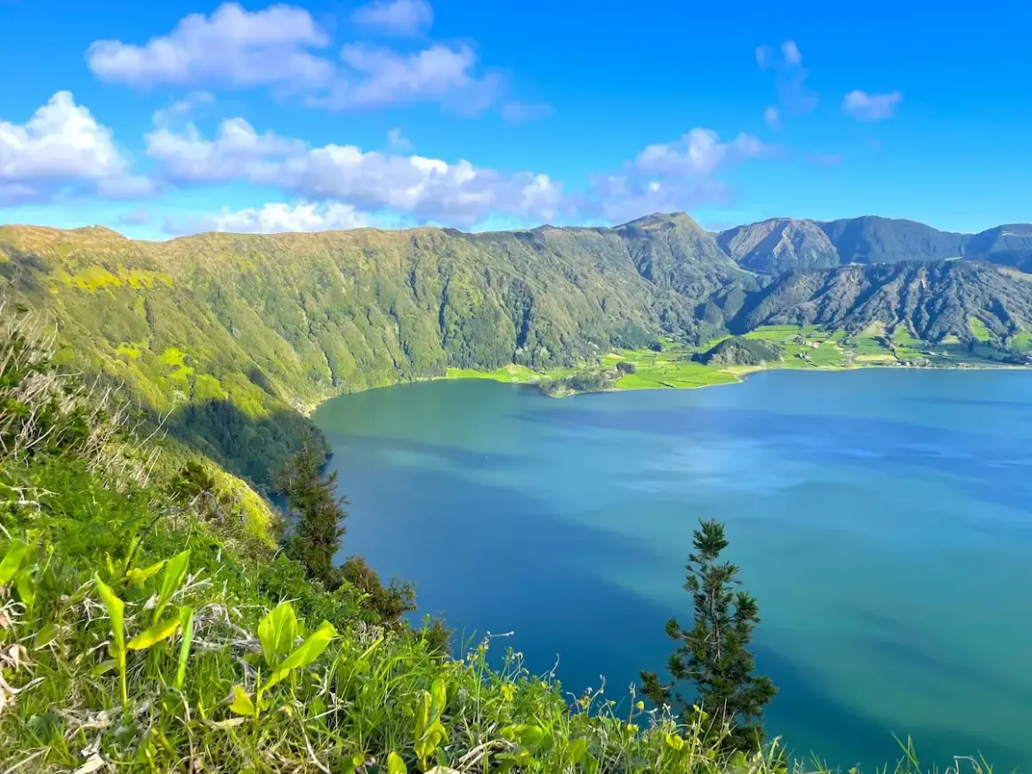 Vue panoramique sur le lac d'une beauté saisissante à São Miguel, entouré de montagnes verdoyantes sous un ciel bleu éclatant.