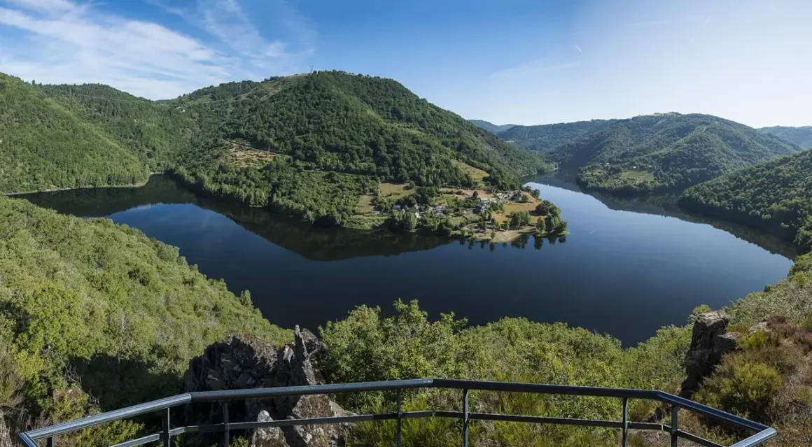 Vue panoramique des gorges de la Truyère, un lac paisible serpente entre des collines verdoyantes. Idéal pour la randonnée.