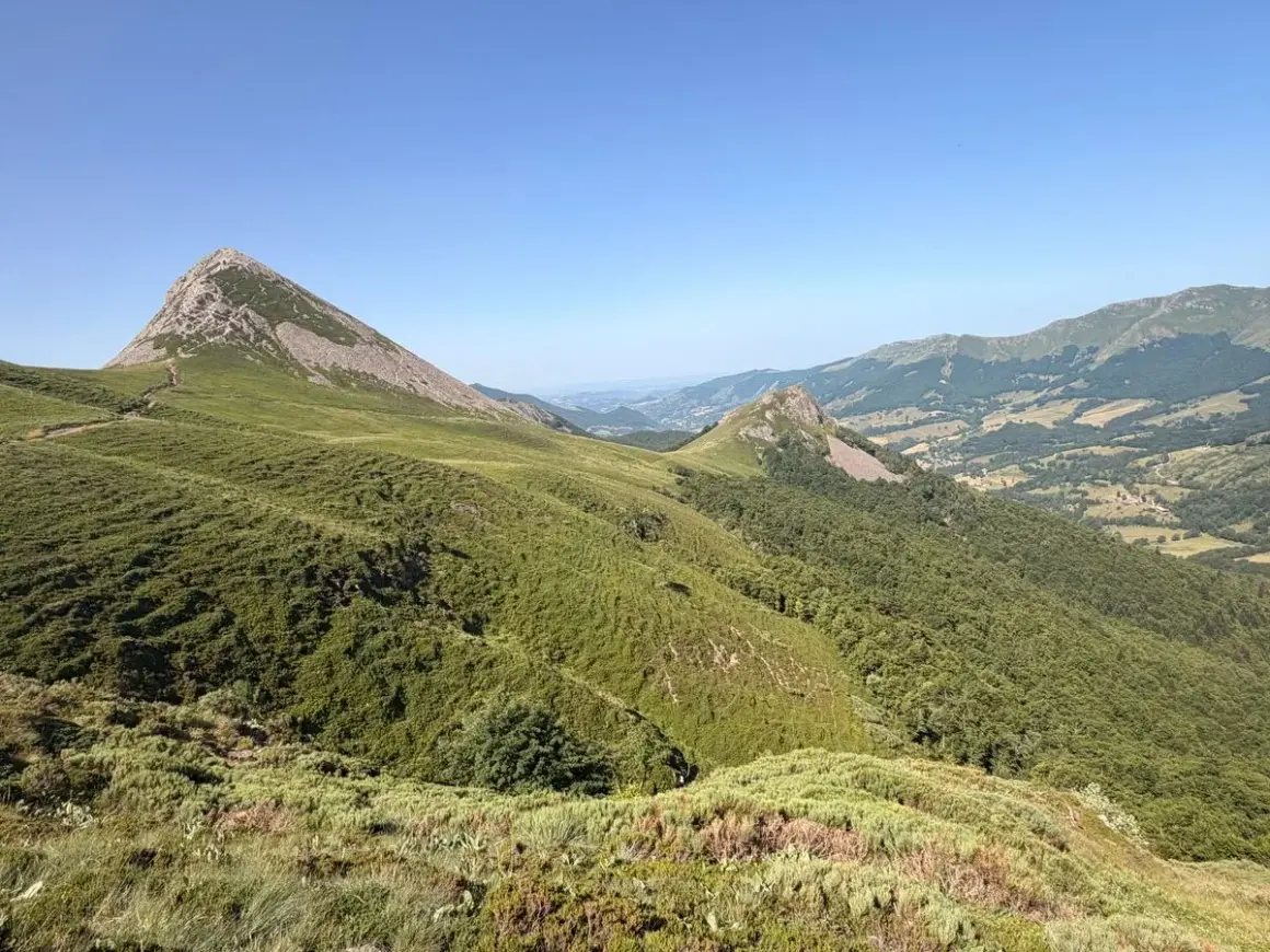 Vue panoramique sur le Puy Griou, sommet emblématique du Cantal, avec ses pentes verdoyantes et rocheuses sous un ciel bleu.