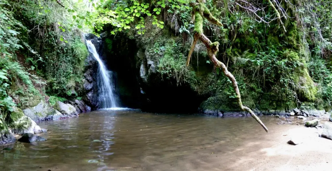 Cascade d'eau tombant dans un bassin aux gorges d'Enval, entourée de végétation luxuriante et de rochers moussus.