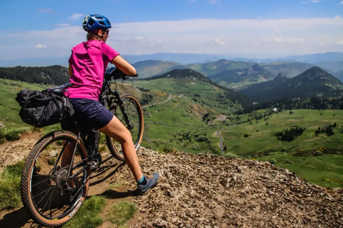 Cycliste au col de la Croix de Boutières, admirant le paysage verdoyant et vallonné. Sacoche sur le vélo, prête pour l'aventure.
