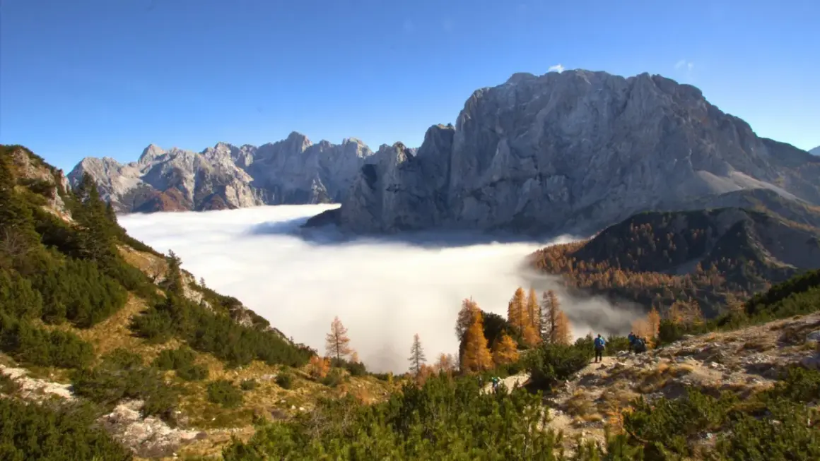 Vue spectaculaire des Alpes Juliennes, avec une mer de nuages enveloppant les vallées et des montagnes majestueuses sous un ciel bleu.