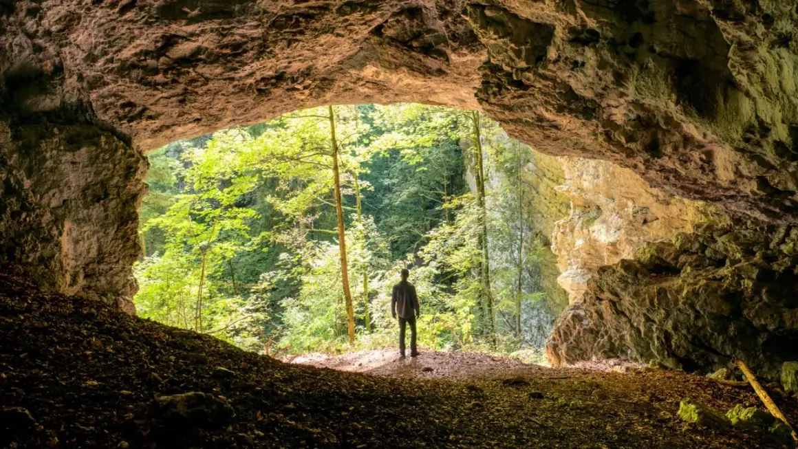 Un homme se tient à l'entrée d'une grotte, contemplant la verdure luxuriante de la gorge de Pokljuka.