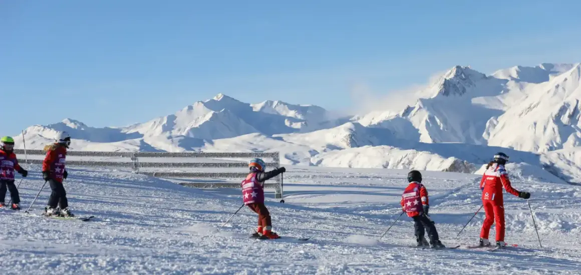 Enfants en plein cours de ski, profitant d'une journée ensoleillée avec des montagnes enneigées en arrière-plan.