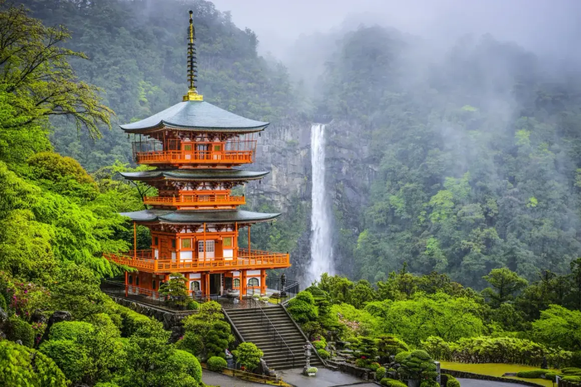 Pagode à trois étages de couleur orange vif, niché dans une végétation luxuriante sur la péninsule de Kii, avec une cascade majestueuse en arrière-plan.