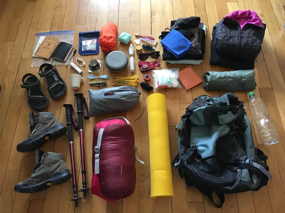 Préparation pour une aventure : chaussures de randonnée, sac de couchage, matelas, vêtements, gourde et accessoires pour savoir comment ranger son sac de randonnée.