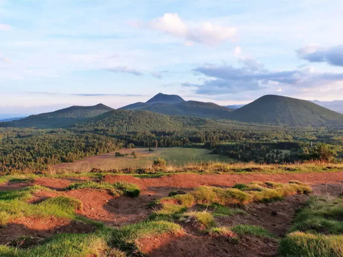 Vue panoramique sur les volcans d'Auvergne, avec le Puy Chopine dominant la forêt verdoyante sous un ciel nuageux.