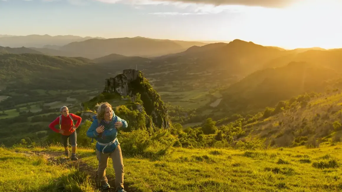 Deux randonneurs sur le sentier des cathares, profitant d'un paysage montagneux baigné par le soleil couchant.