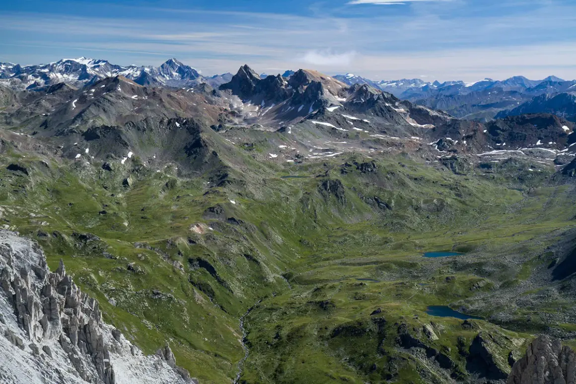 Vue panoramique des Alpes, avec le Mont Thabor en arrière-plan. Des lacs bleus scintillent dans la vallée verdoyante.