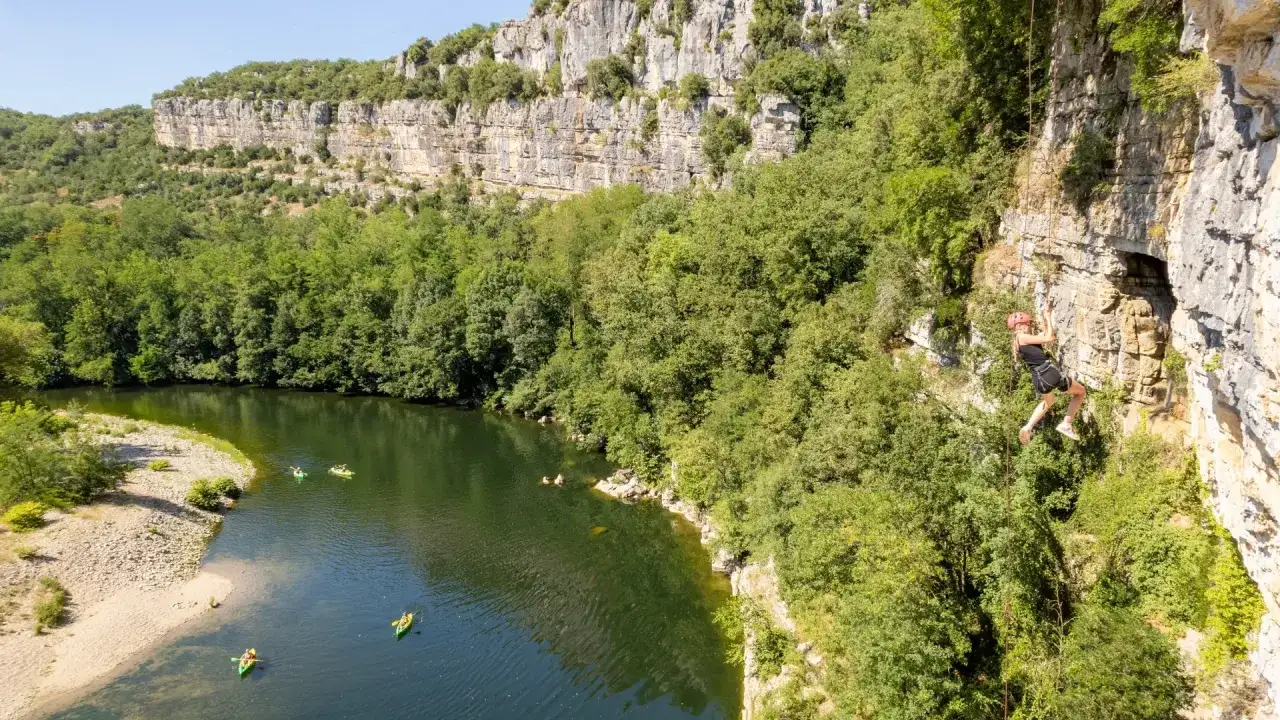 Escalade dans les gorges du Chassezac, avec un kayakiste descendant la rivi&egrave;re.