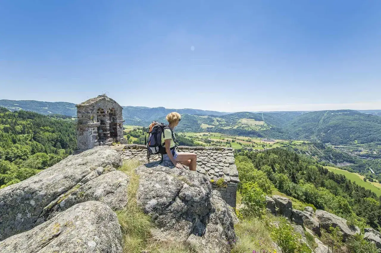Randonneuse admirant le paysage verdoyant de la gorge de l'Allier depuis un promontoire rocheux, avec une petite b&acirc;tisse en pierre &agrave; proximit&eacute;.