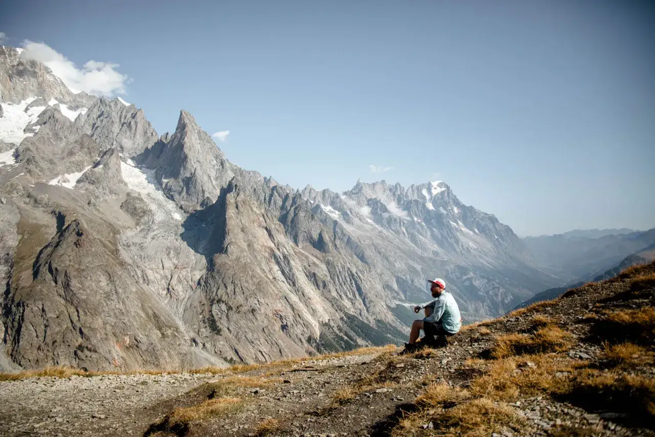 Un randonneur profite d'une pause sur le parcours Mont-Blanc, contemplant les majestueuses montagnes enneigées.