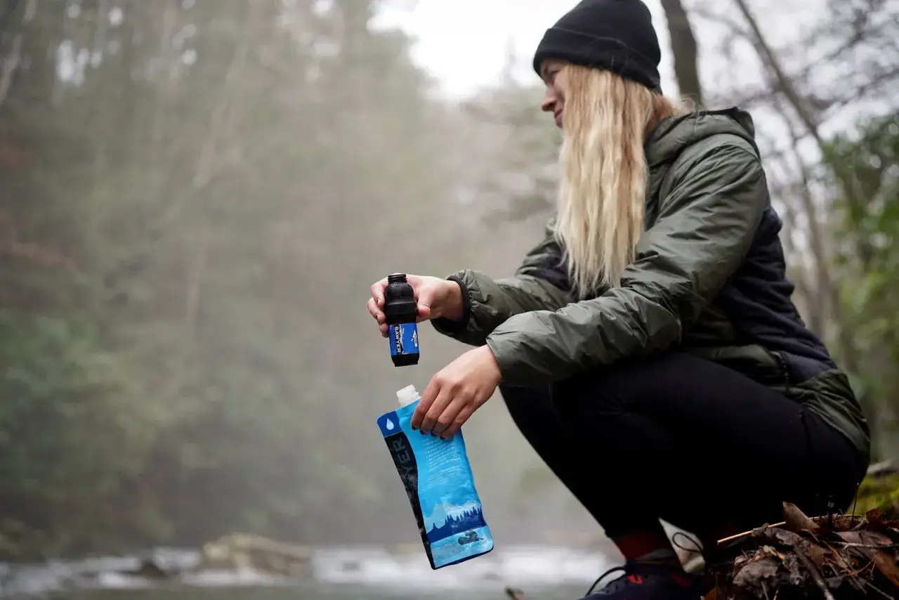 Une randonneuse utilise une pastille de chlore pour eau potable Sawyer pr&egrave;s d'un ruisseau.