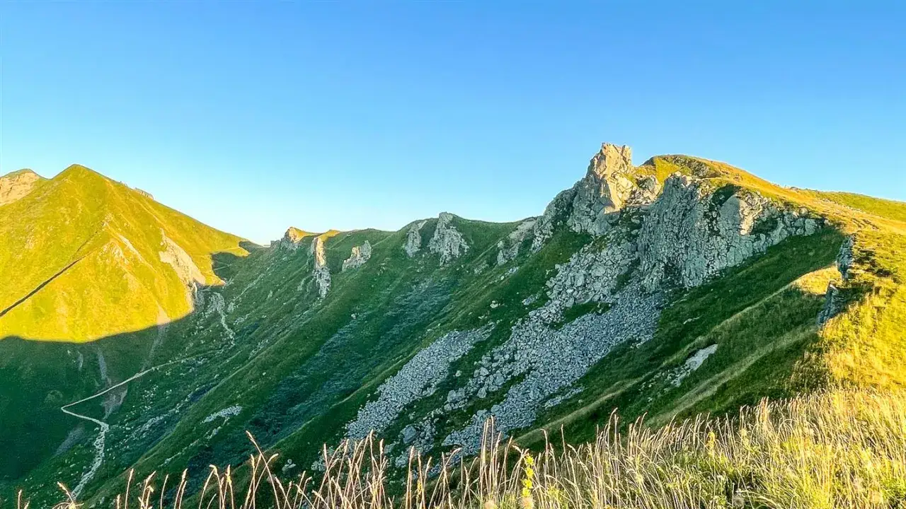 Le cirque de la fontaine salée, un paysage montagneux verdoyant baigné de soleil, avec des rochers escarpés et un ciel bleu clair.