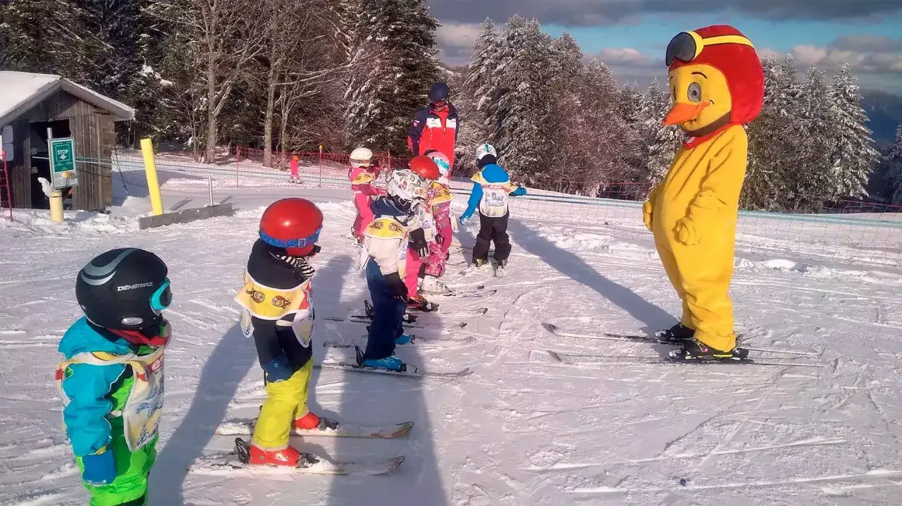 Des enfants en plein cours de ski, encadr&eacute;s par un moniteur et une mascotte rigolote.